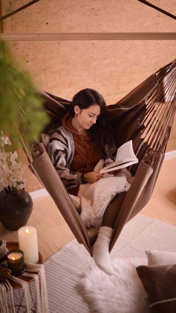 Kobieta czytająca książkę w fotelu hamakowym.